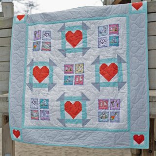 Das Bild zeigt die Kinderdecke From The Heart mit roten Herzen in Patchworktechnik und kleinen Quadraten mit liebevollen Tiermotiven.