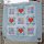 Das Bild zeigt die Kinderdecke From The Heart mit roten Herzen in Patchworktechnik und kleinen Quadraten mit liebevollen Tiermotiven.