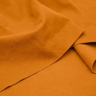 Das Bild zeigt den Heavy Washed Canvasstoff in carrot. Es ist ein helles orange. Der Stoff liegt leicht aufgefaechert auf einem Tisch.