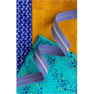 Das Bild zeigt den Endlos-Reissverschluss blau weisse Streifen mit nickelfarbenen Zaehnen. Dekoriert ist er vor einer Vielzahl an bunten Stoffen.