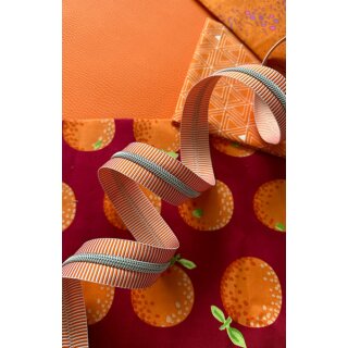 Das Bild zeigt den Endlos-Reissverschluss orange weisse Streifen mit nickelfarbenen Zaehnen. Dekoriert ist er vor einer Vielzahl an bunten Stoffen.