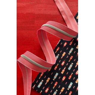 Das Bild zeigt den Endlos-Reissverschluss rot weisse Streifen mit nickelfarbenen Zaehnen. Dekoriert ist er vor einer Vielzahl an bunten Stoffen.